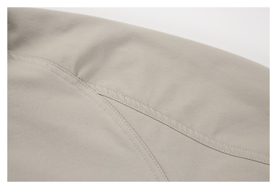 Close-up of the light taupe jacket's curved shoulder seam and stitching.