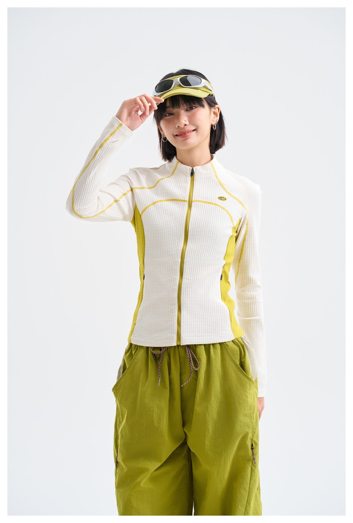 Model wearing a white textured zip-up jacket with yellow piping and side panels, paired with olive pants.