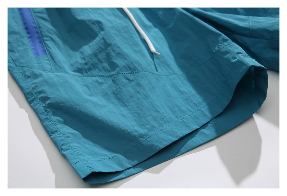 Close-up of the teal shorts' stitched hem, with part of a white drawcord and blue pocket visible.