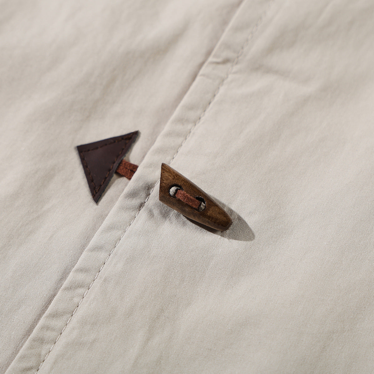 Close-up of a beige shirt's toggle fastening, with a brown wooden toggle and triangular tab.