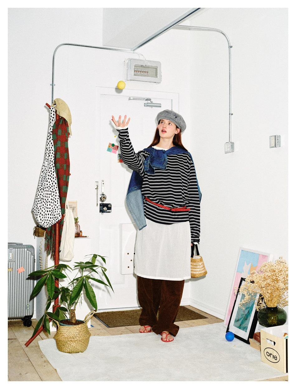 Full-length model wearing a black-and-white striped top, white apron-style layer, red belt and denim draped over her