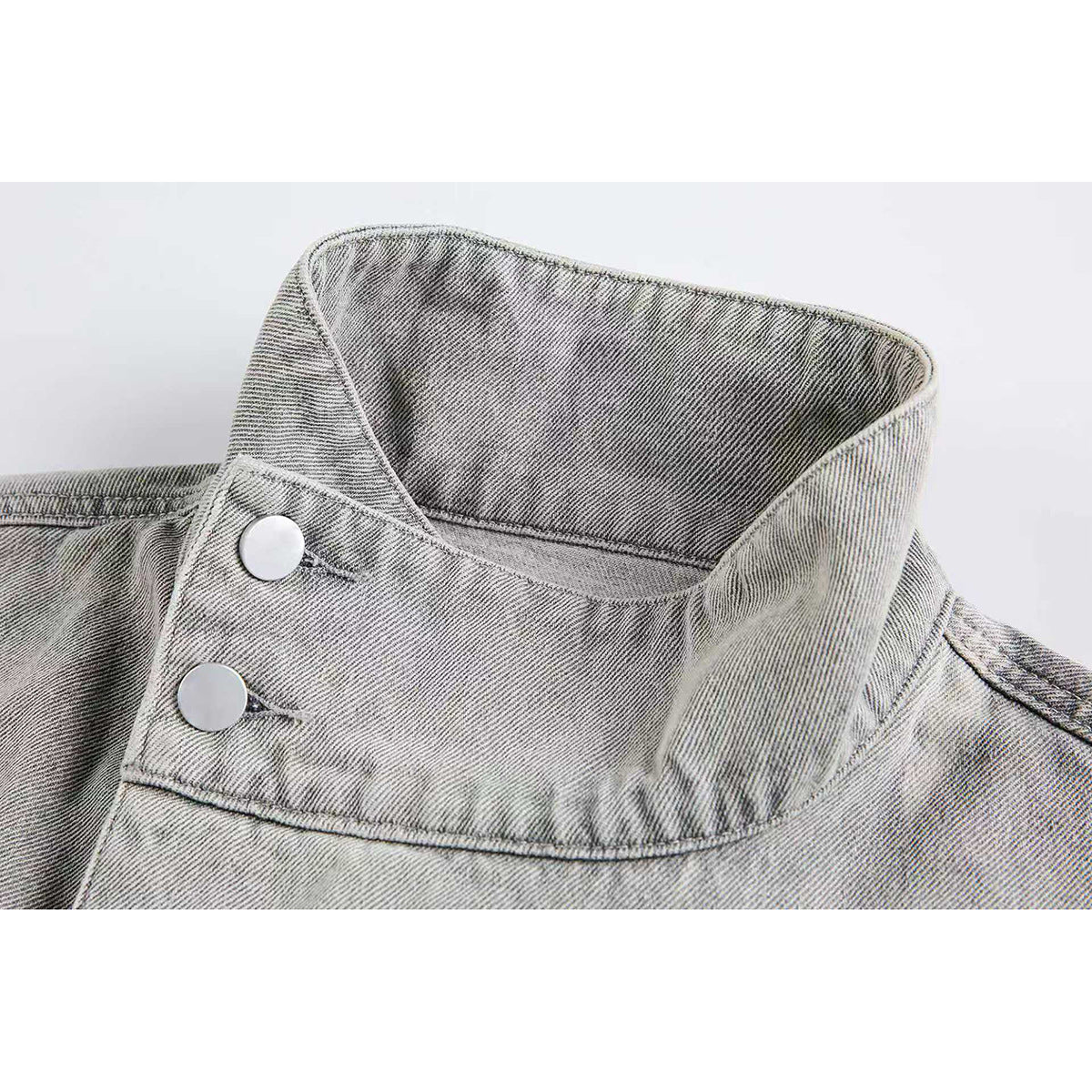 Close-up of a light gray jacket’s tall collar and two silver snap buttons.
