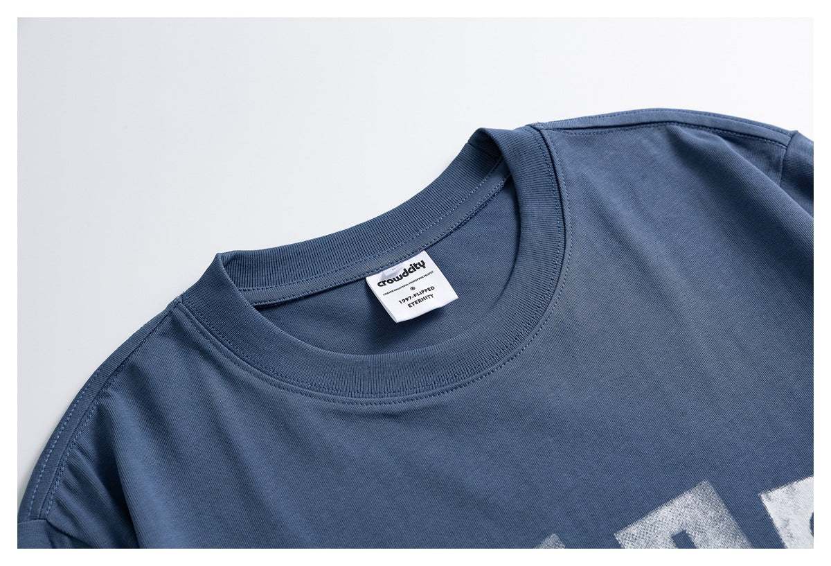 Close-up of a slate-blue T-shirt's ribbed crew neck, inner label, and partial white graphic.