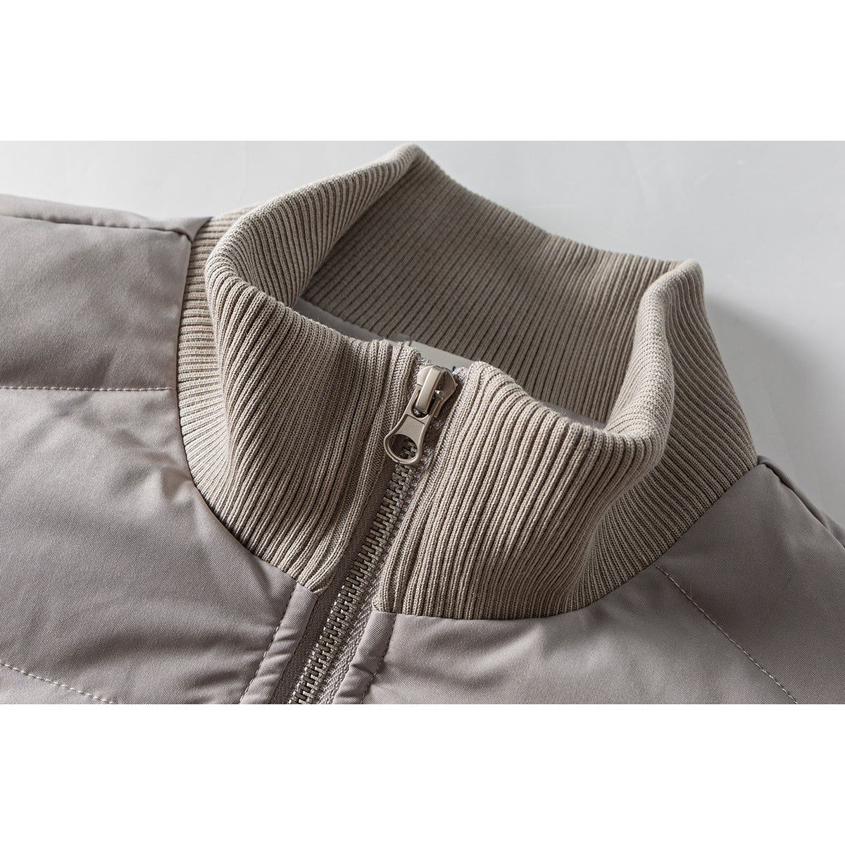 Close-up of a light gray jacket's ribbed stand collar and front zipper.