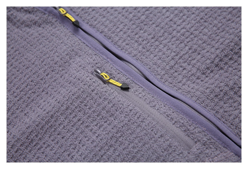 Close-up of a gray textured garment with a diagonal zipper and yellow-and-black zipper pulls.