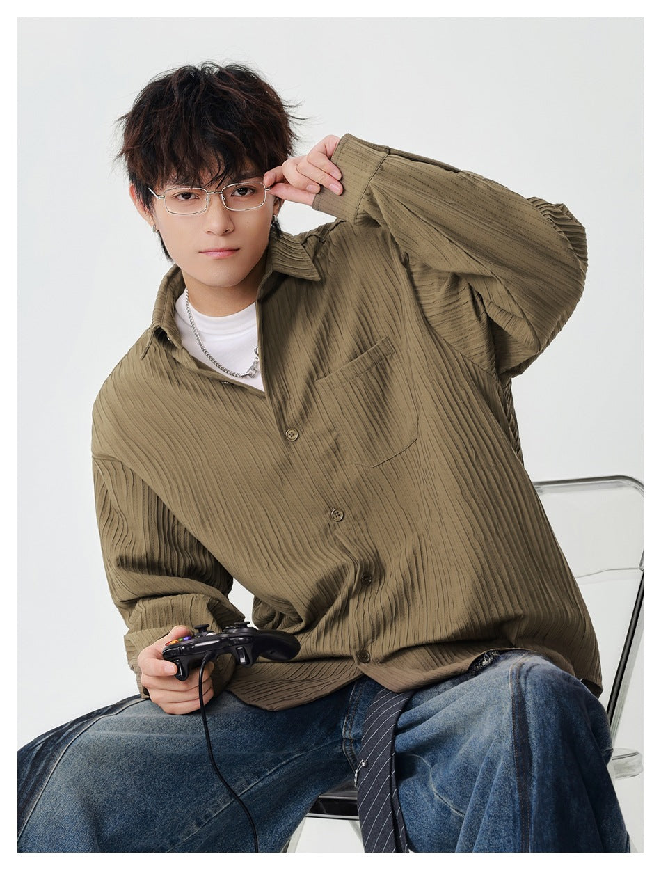 Seated model wearing a khaki textured-stripe button shirt over a white tee with jeans, one hand raised to glasses