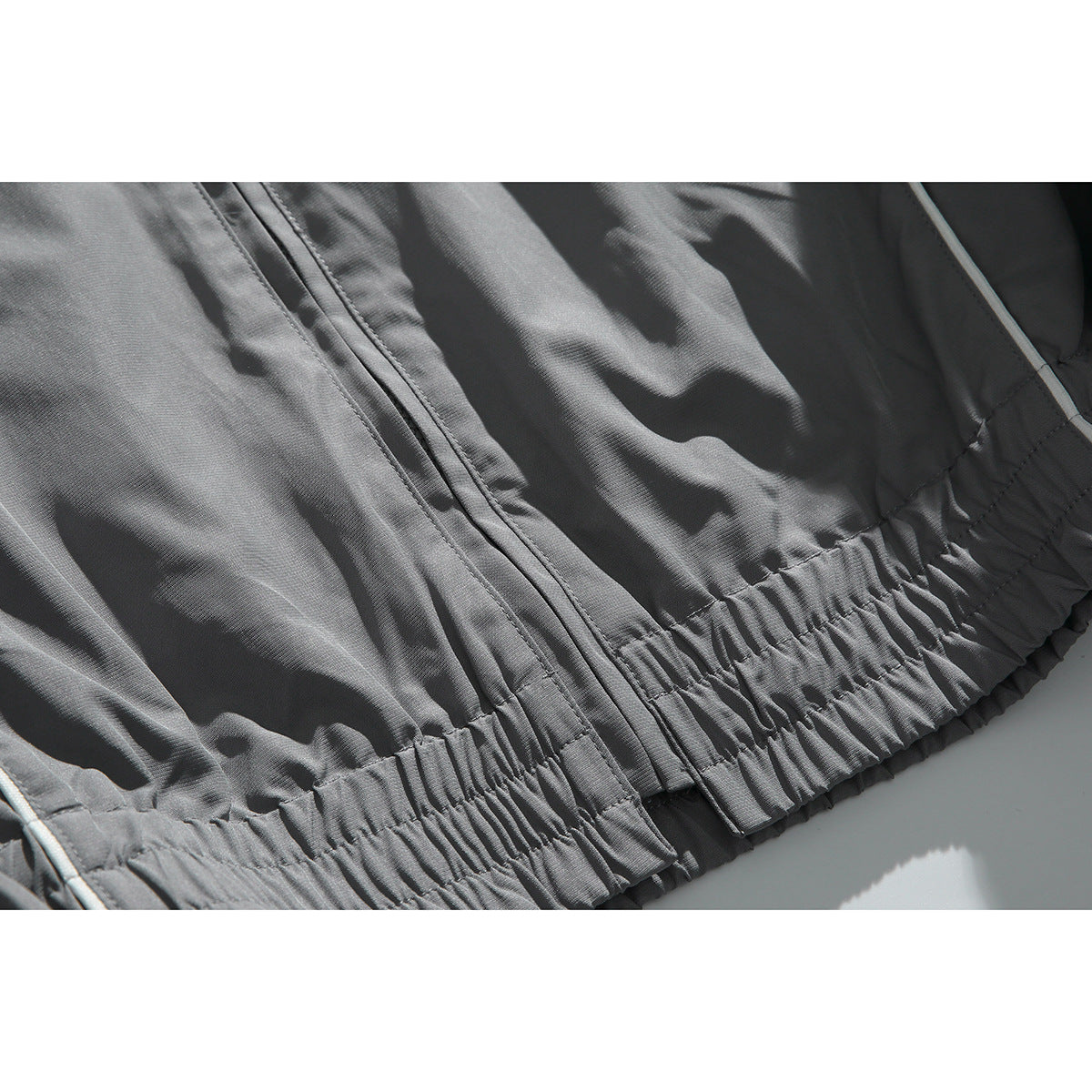 Close-up of a charcoal jacket's front zipper and gathered elastic hem.