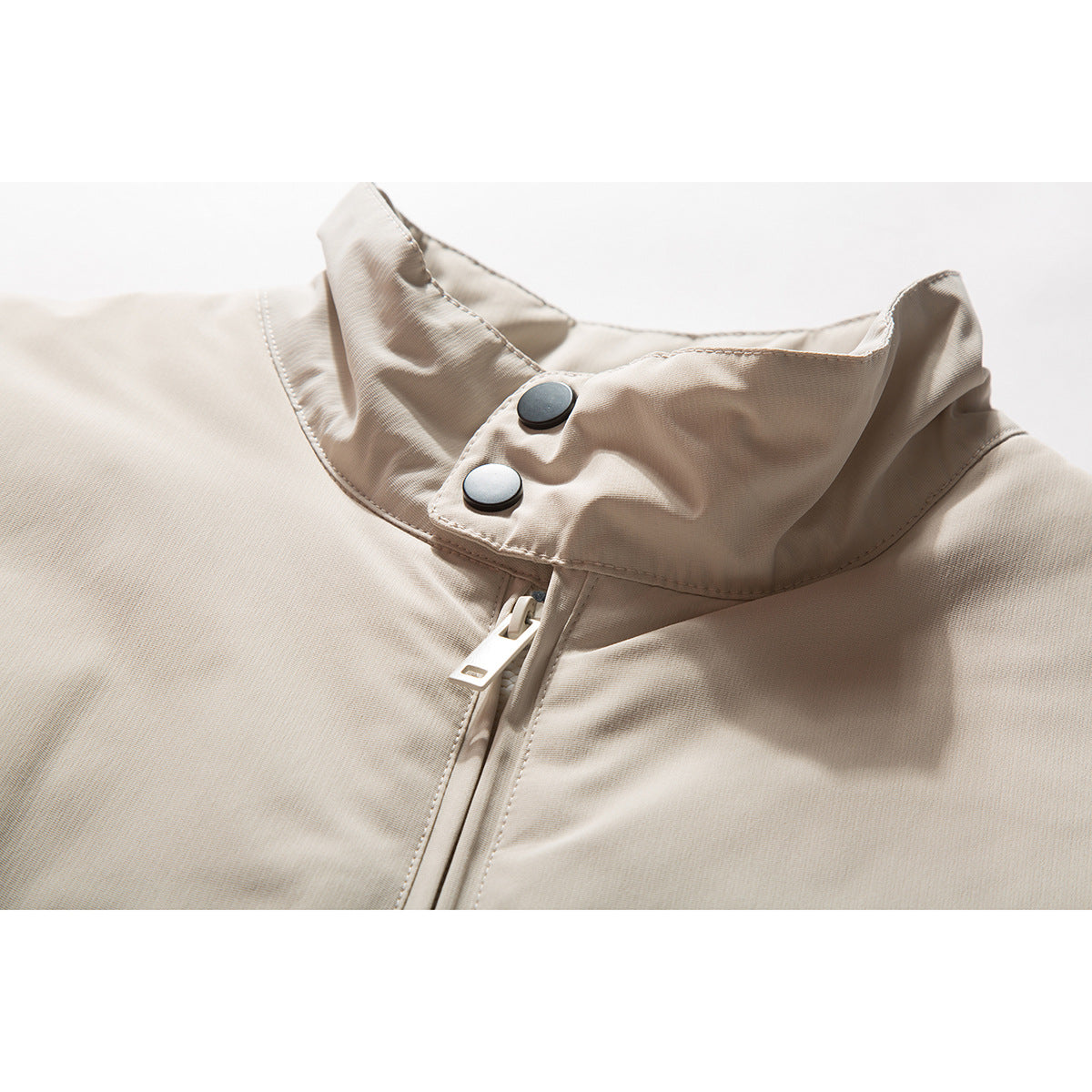 Close-up of a beige jacket's raised collar, two dark snaps, and front zipper.