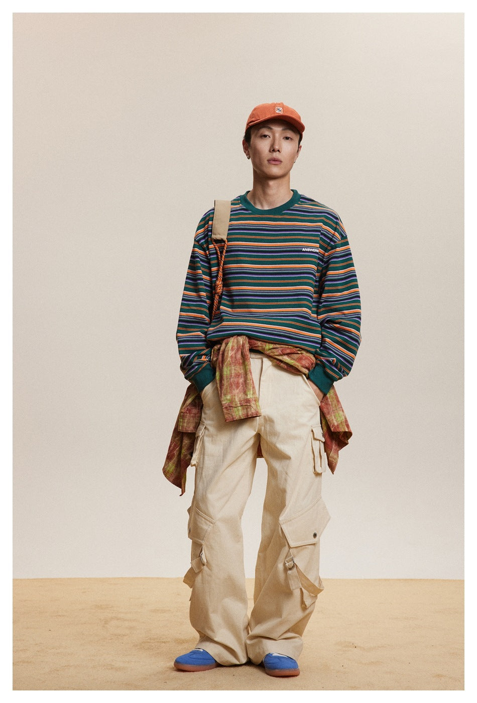 A standing model wears a green long-sleeve shirt with orange, purple, and light-colored horizontal stripes.