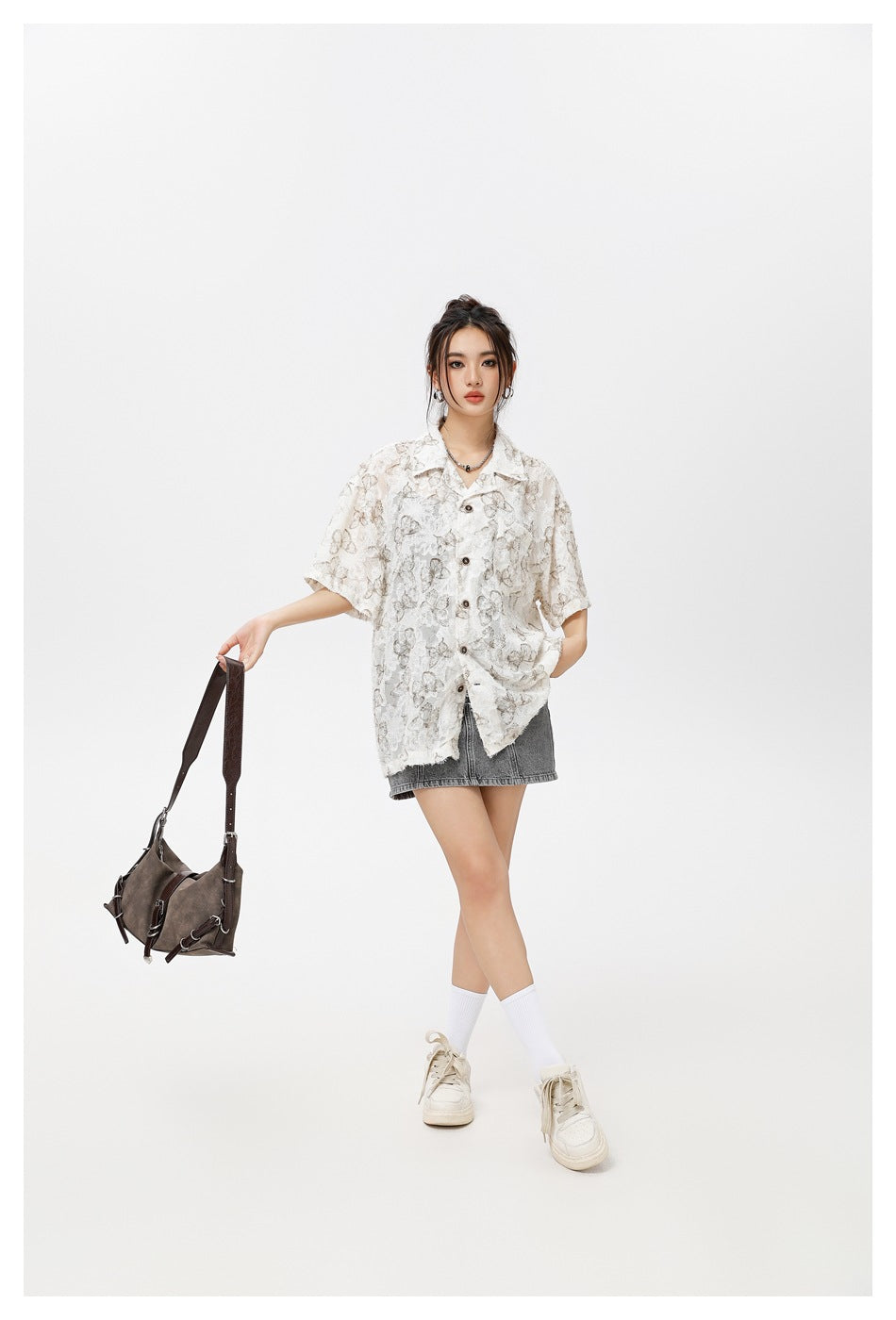 Model wearing an oversized white butterfly-print shirt with a gray denim mini skirt and holding a dark shoulder bag.