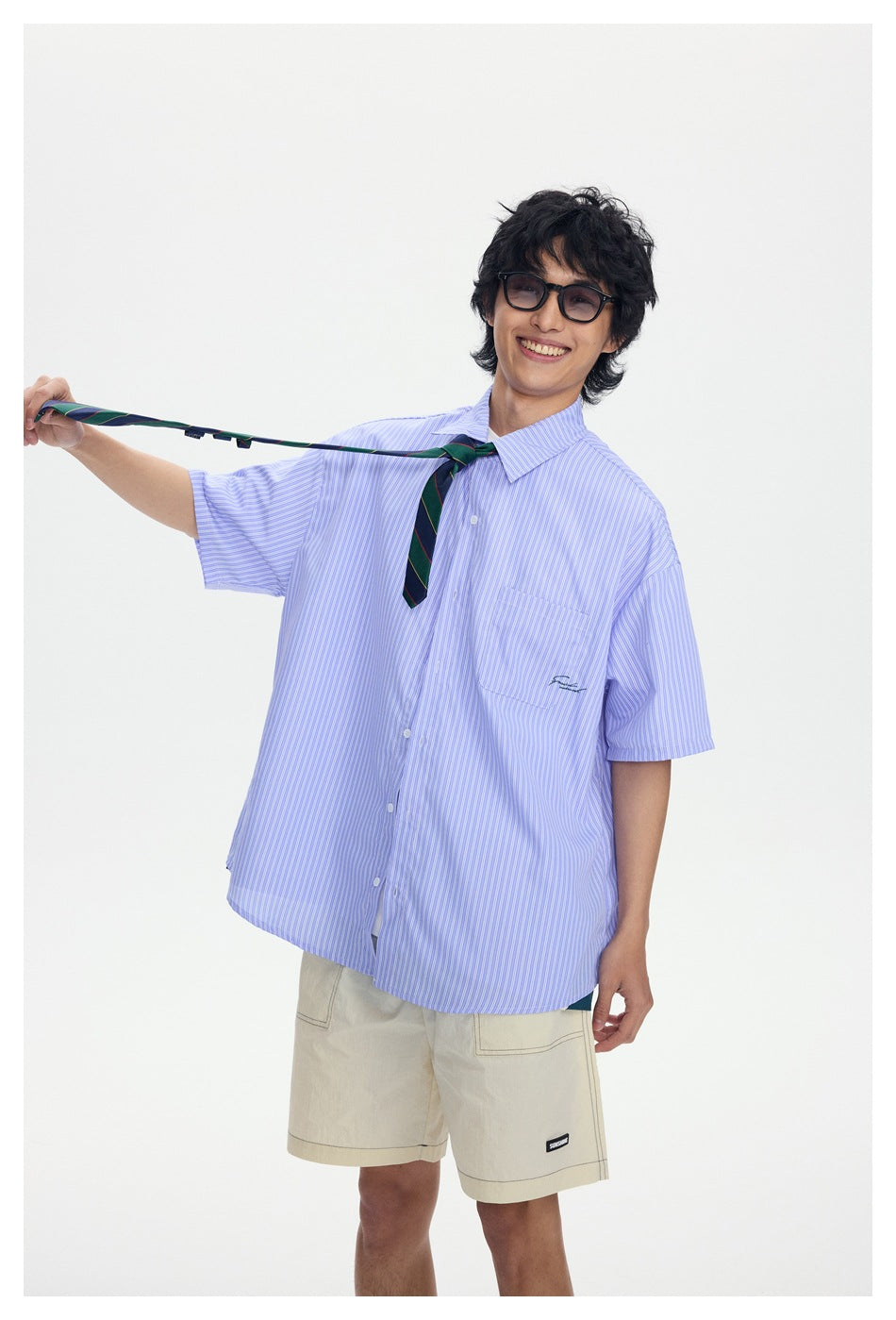 Model wearing a loose blue-and-white striped short-sleeve button-up shirt with a chest pocket and khaki shorts.