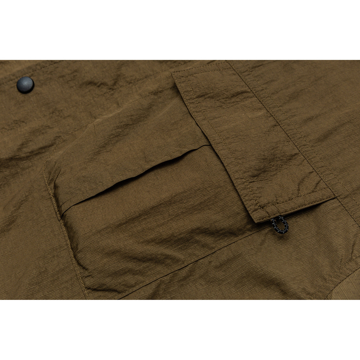 Close-up of an olive-brown jacket pocket with a flap, black snap button, and narrow tab with a loop.