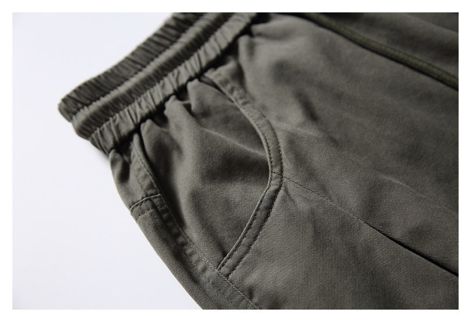 Close-up of dark olive-gray pants showing the elastic waistband and curved side pocket.