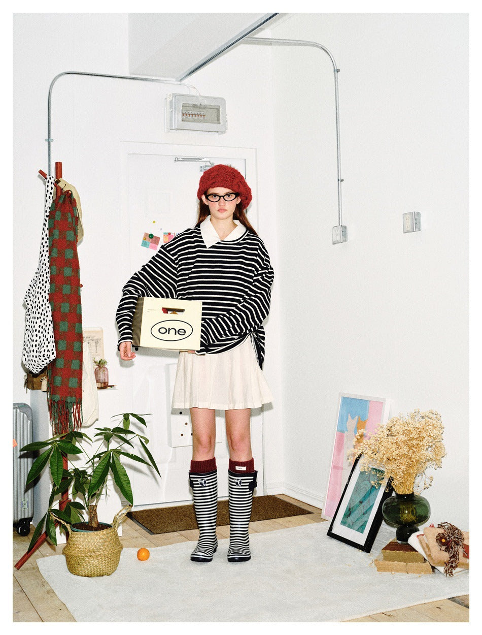 Front view of a model wearing a black-and-white striped oversized sweater with a white collar and cream pleated skirt.