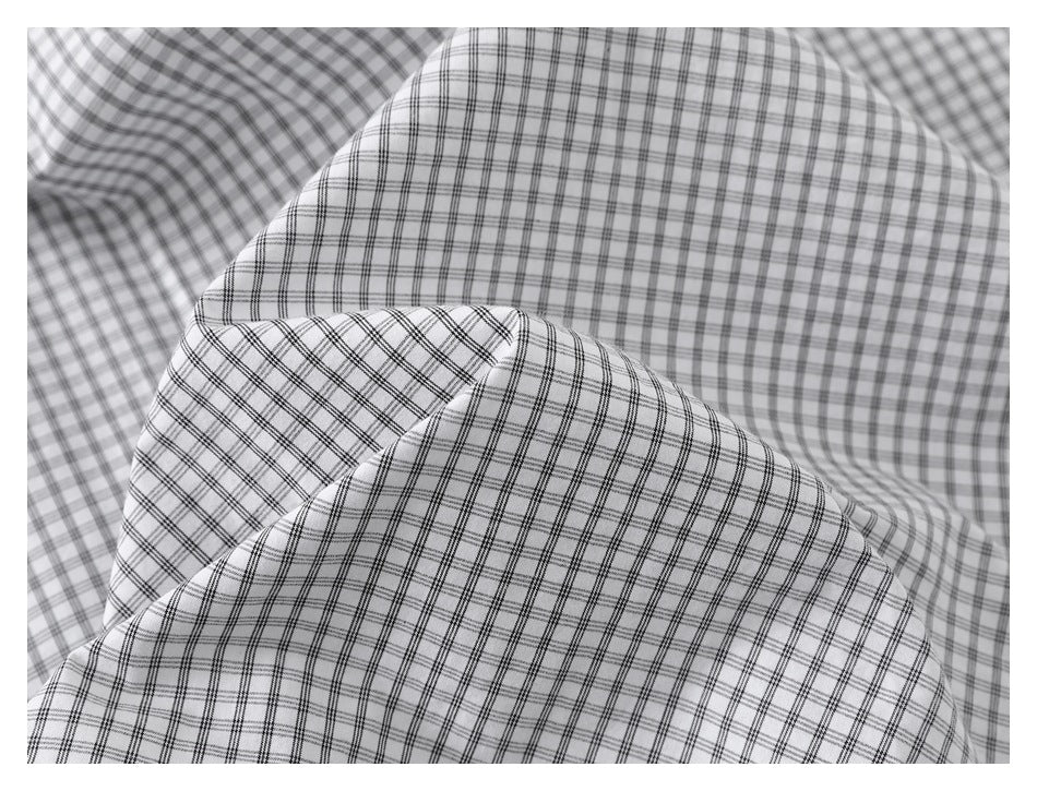 Close-up of the white shirt fabric draped in folds, showing its fine black grid-check pattern.