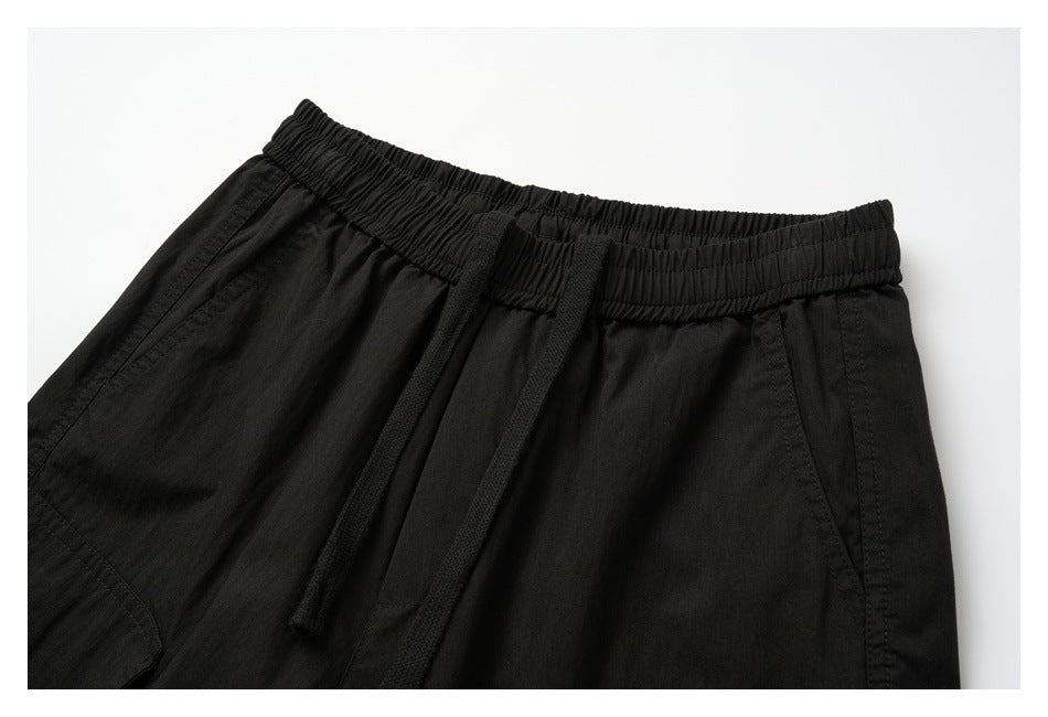 Close-up of black cargo pants showing the elastic waistband, drawstring, and angled front pockets.