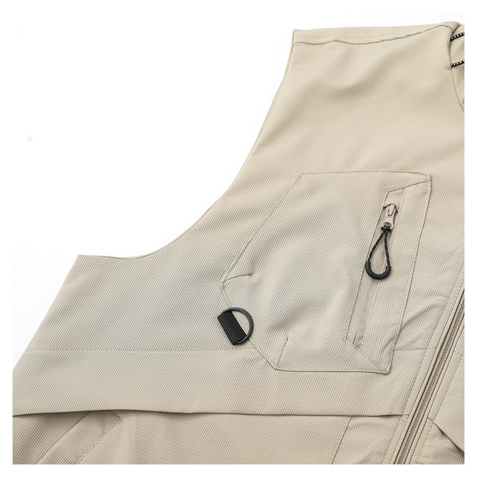 Close-up of a beige vest chest pocket with a vertical zipper, black pull, and adjacent D-ring.