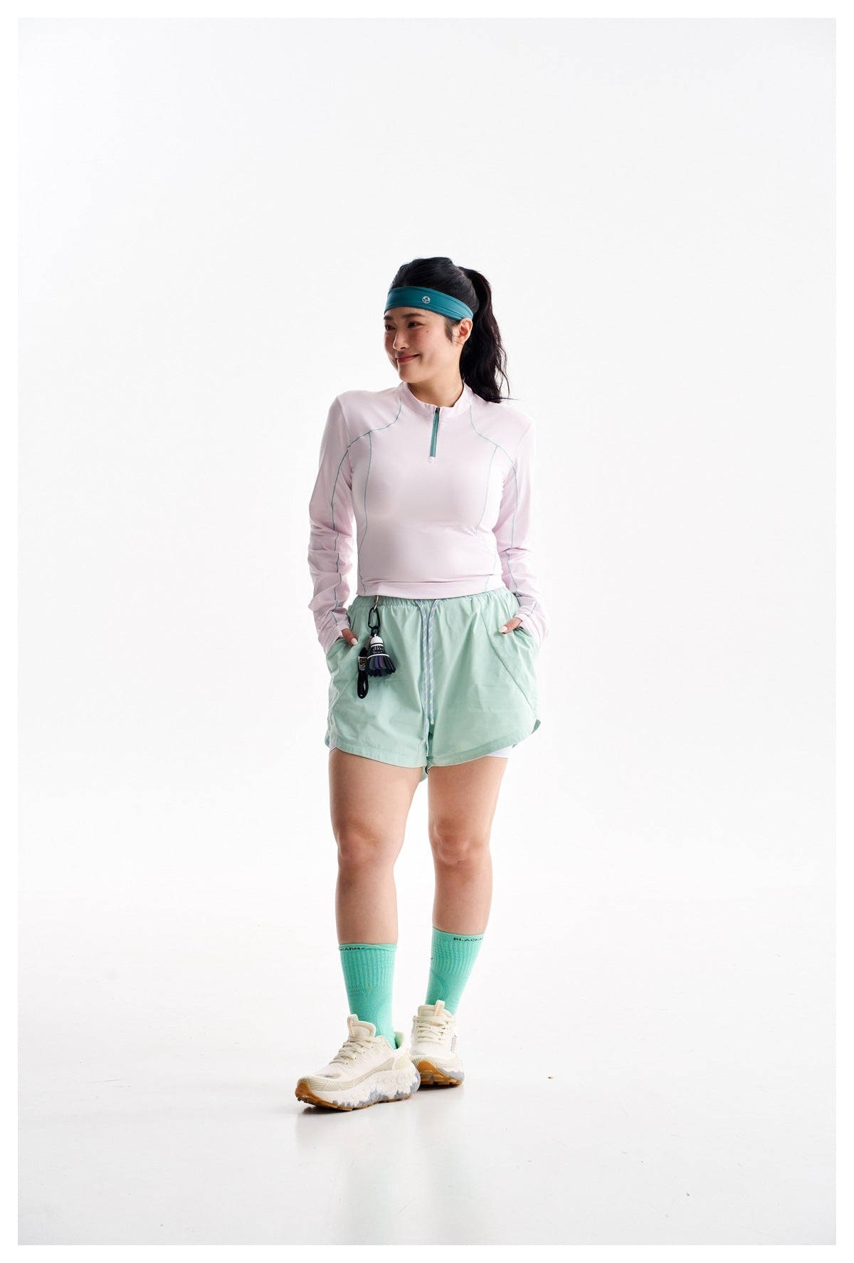 Full-length model wearing a pale pink quarter-zip top, mint shorts, teal socks, and white sneakers.