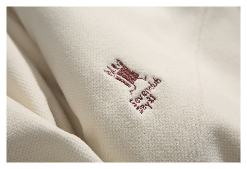 Close-up of a small burgundy embroidered motif and lettering on ivory textured fabric.