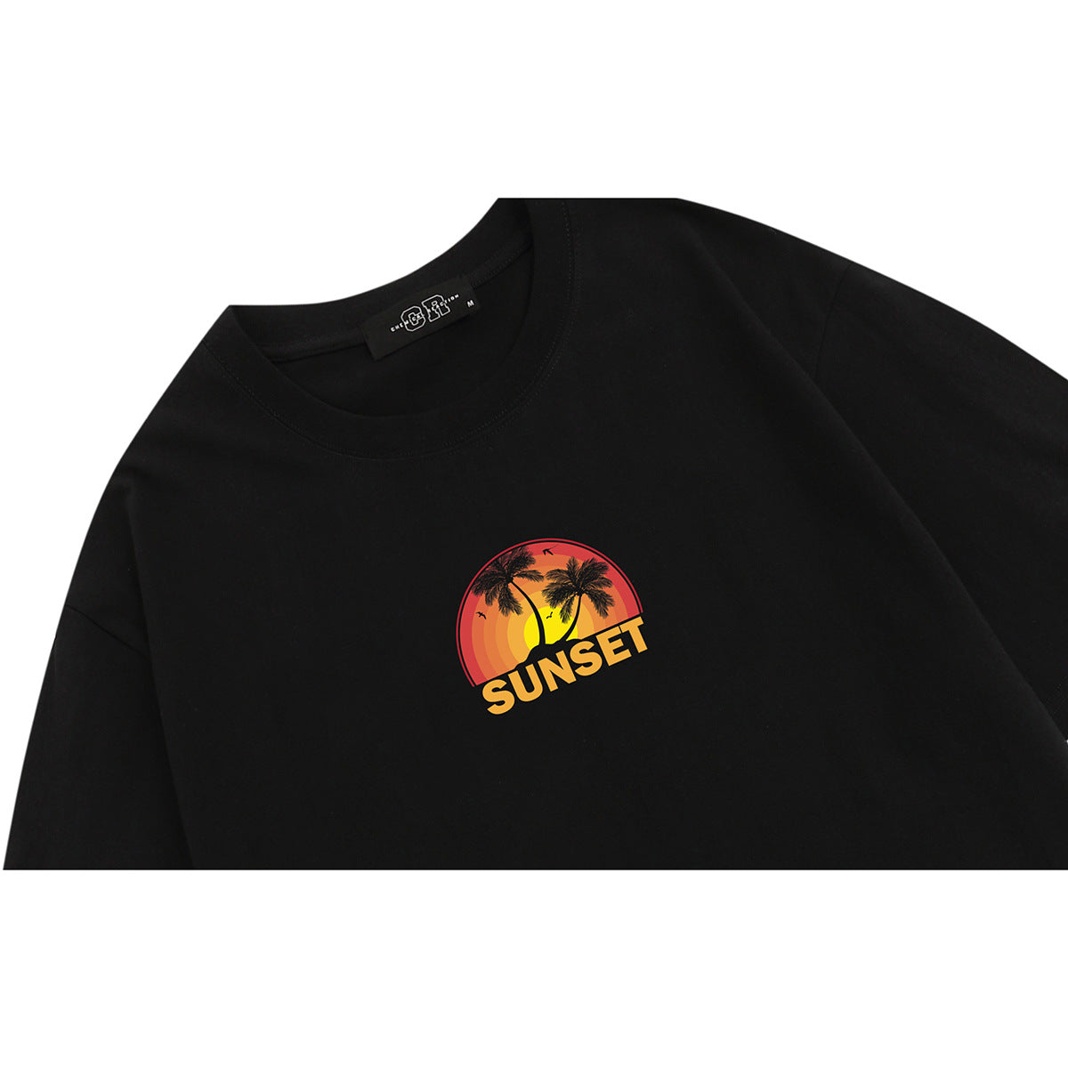 Close-up of a black T-shirt with a small orange sunset and palm tree graphic reading “SUNSET.”
