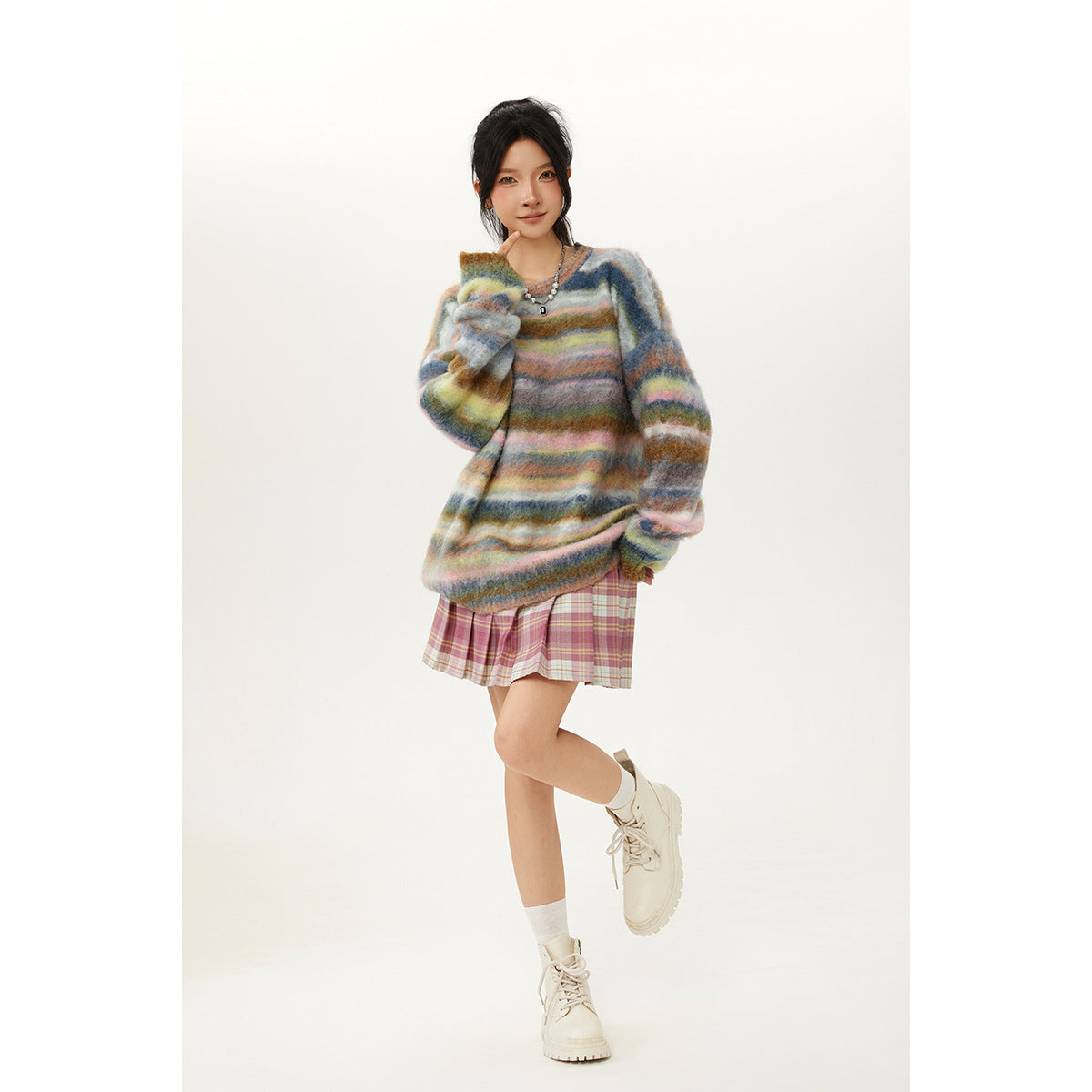 Model wearing an oversized fuzzy sweater with multicolor horizontal stripes, a pink plaid skirt, white socks and boots.