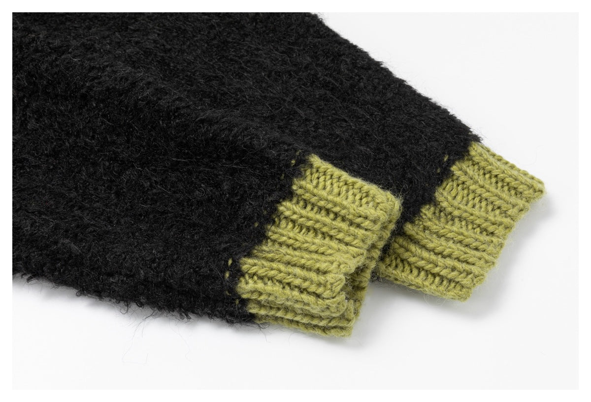 Close-up of black fuzzy knit sleeves with contrasting olive-green ribbed cuffs.