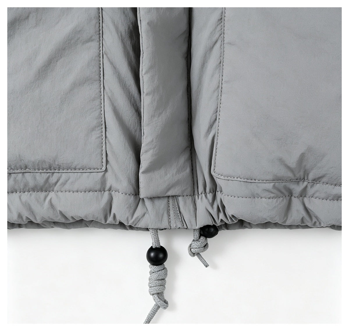 Close-up of a light gray jacket hem with stitched panels and adjustable drawcords with black toggles.