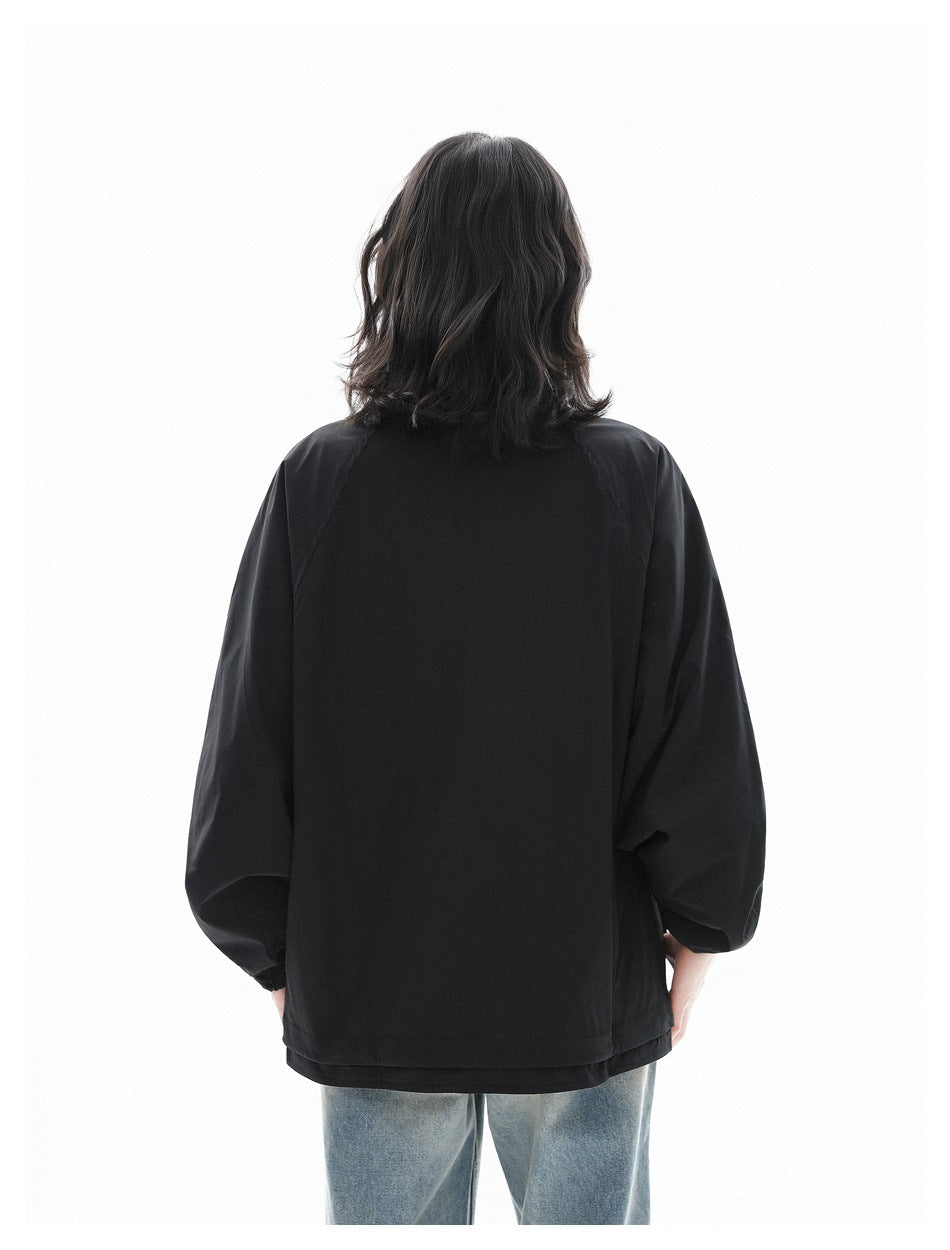 Back view of a model wearing a black raglan-sleeve jacket with light-wash jeans