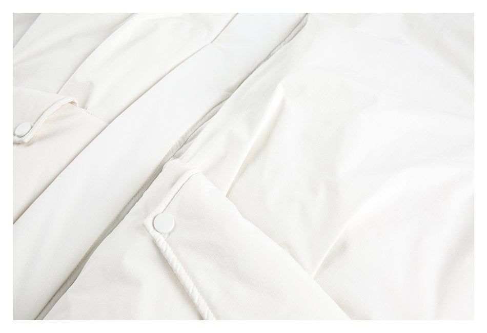 Close-up of an ivory garment's cuff tab, snap button, and adjoining seams.