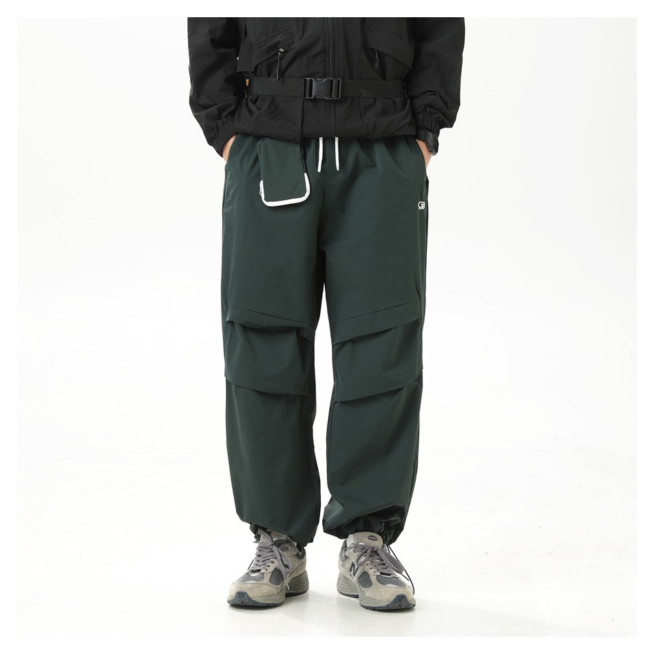 Front view of a model wearing dark green wide-leg cargo pants with layered knee panels, drawstrings, and a white-edged
