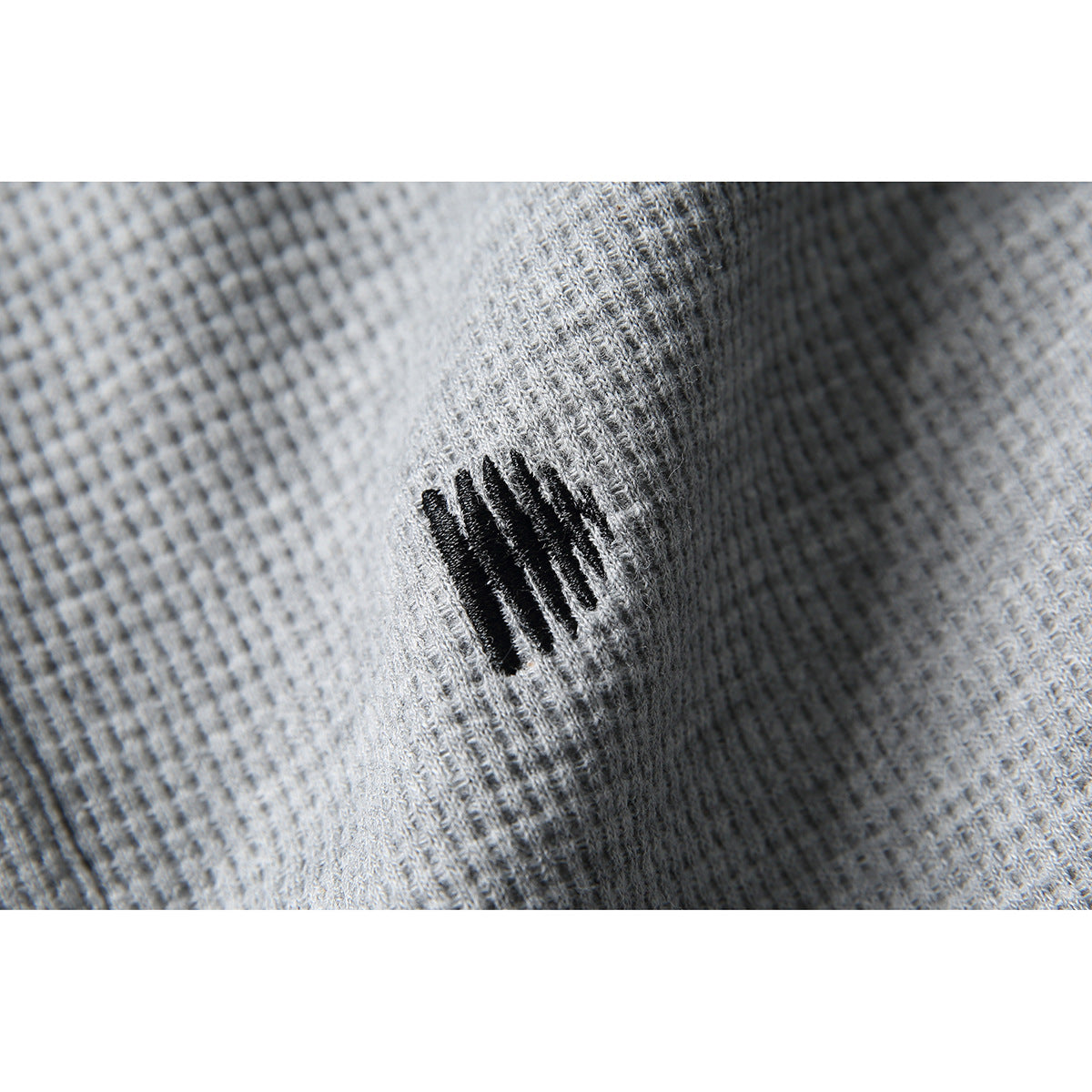 Close-up of a small black embroidered mark on gray textured shirt fabric.