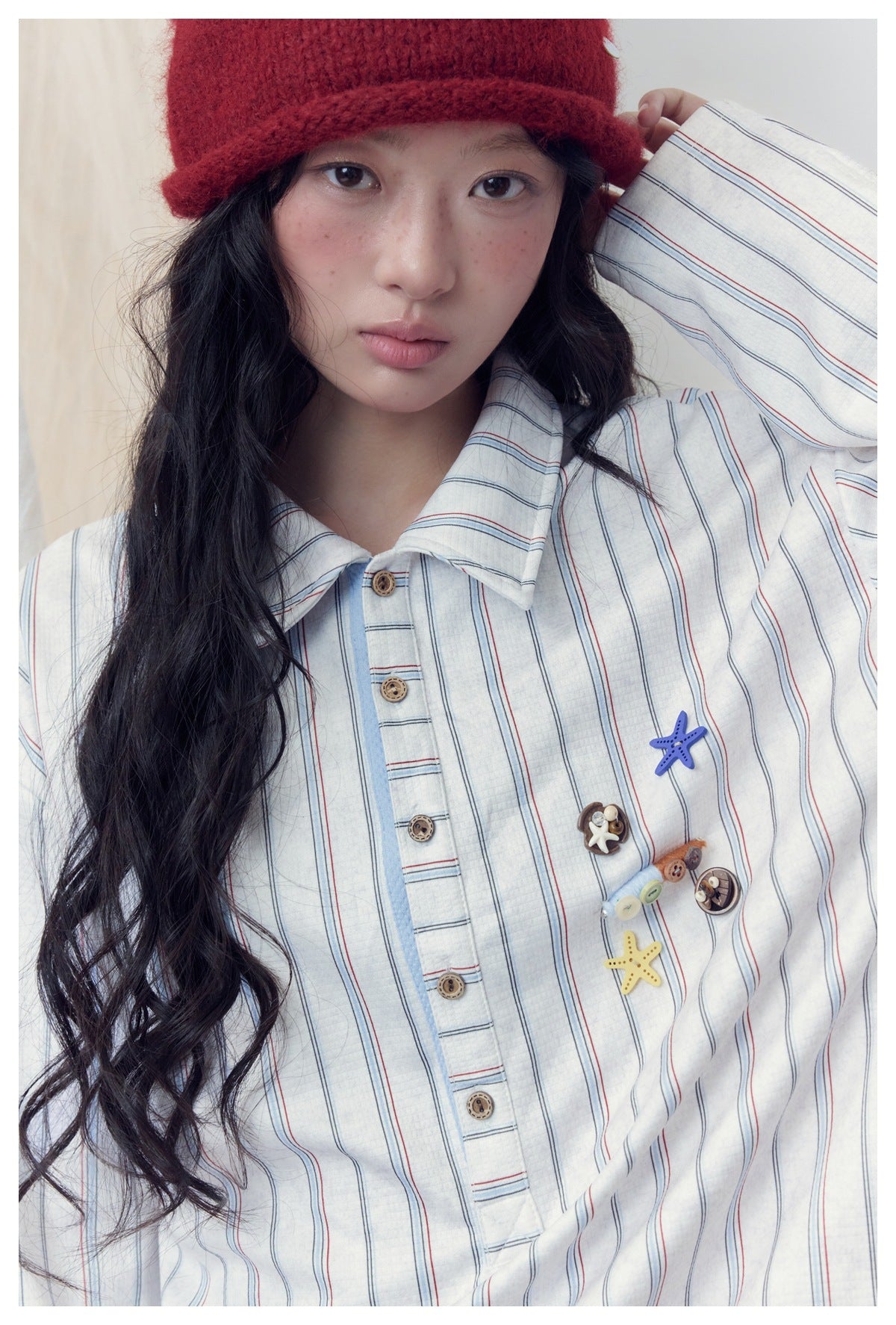 Close-up of a model wearing a striped white shirt with a pointed collar, button placket, and colorful chest embellishments.