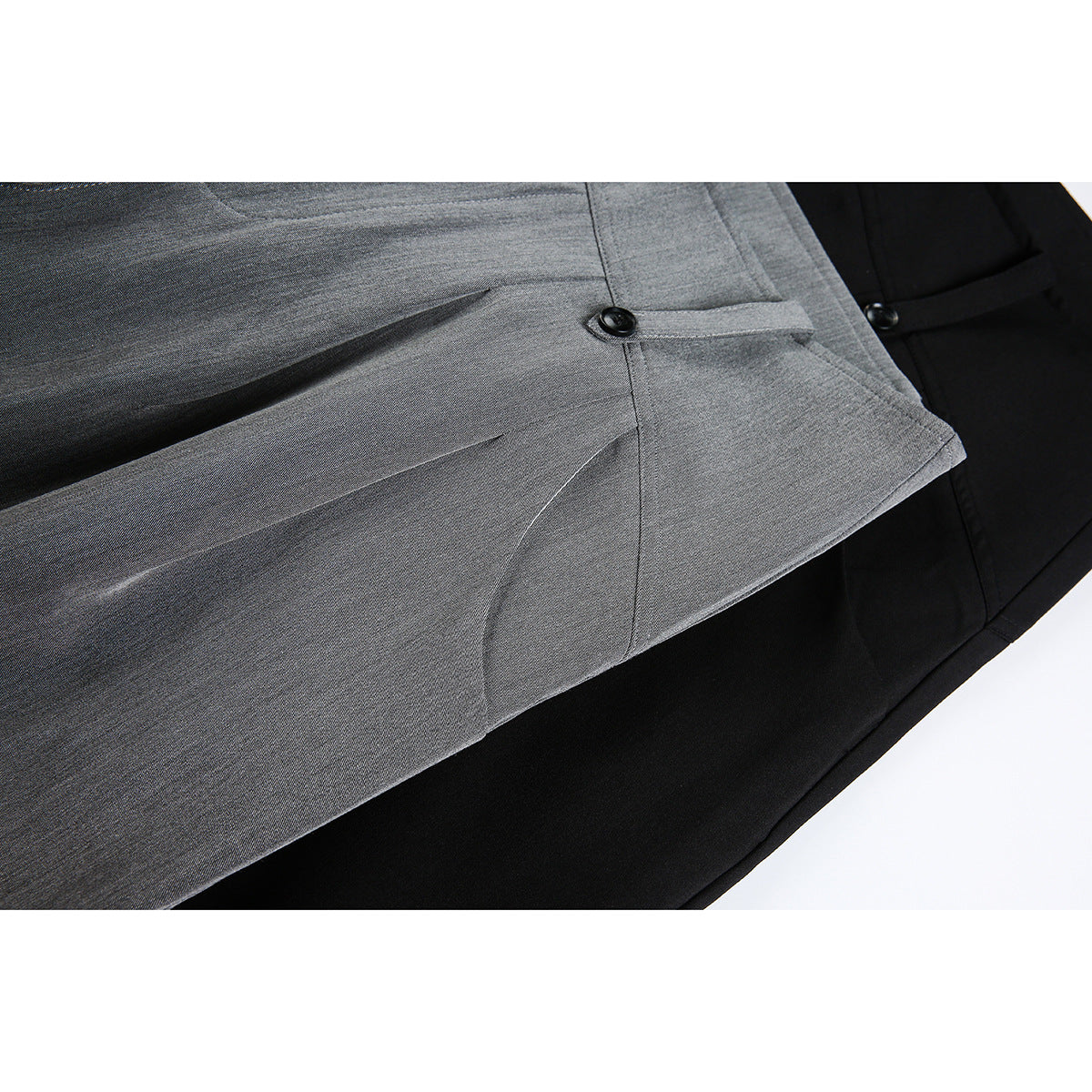 Close-up of gray and black trousers showing a buttoned waist tab, pleats, and pocket seams.