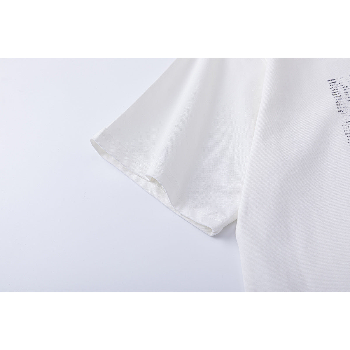 Close-up of a white T-shirt sleeve hem and adjacent fabric, with part of a black printed graphic at the edge.
