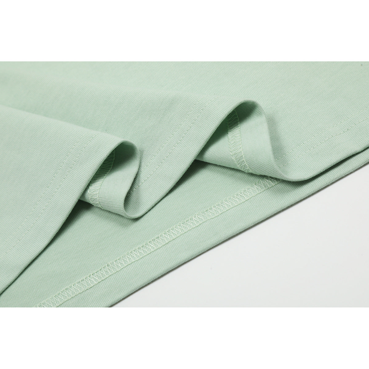 Close-up of the mint green T-shirt hem showing folded fabric and overlock stitching.