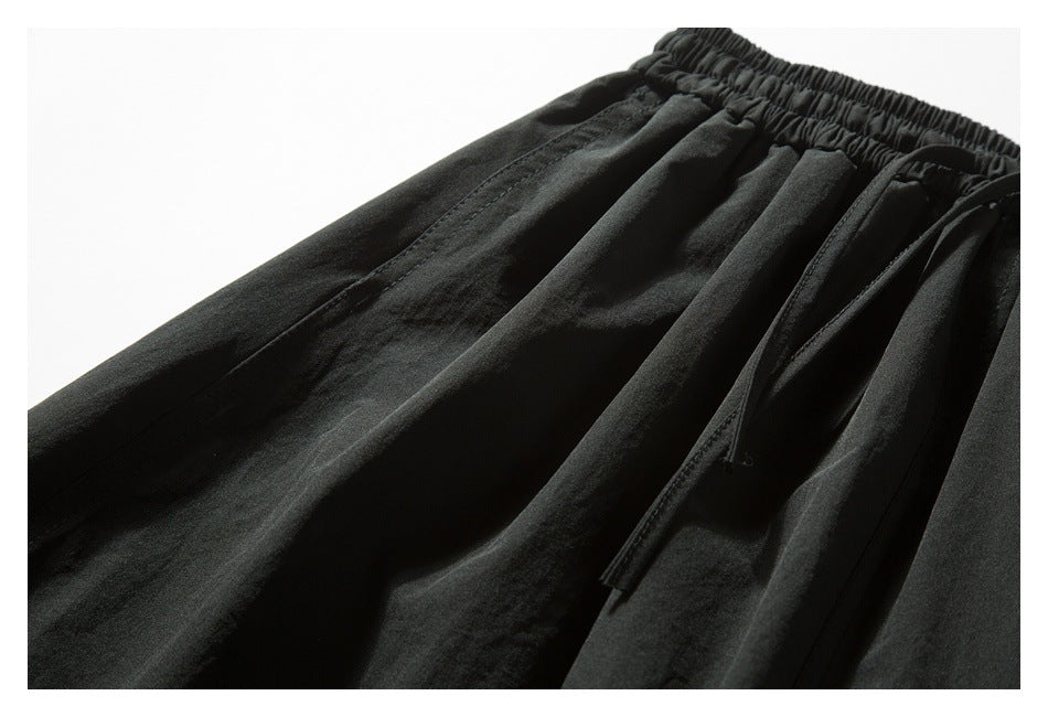 Angled close-up of black gathered waistband, drawstring, and stitched fabric panels.