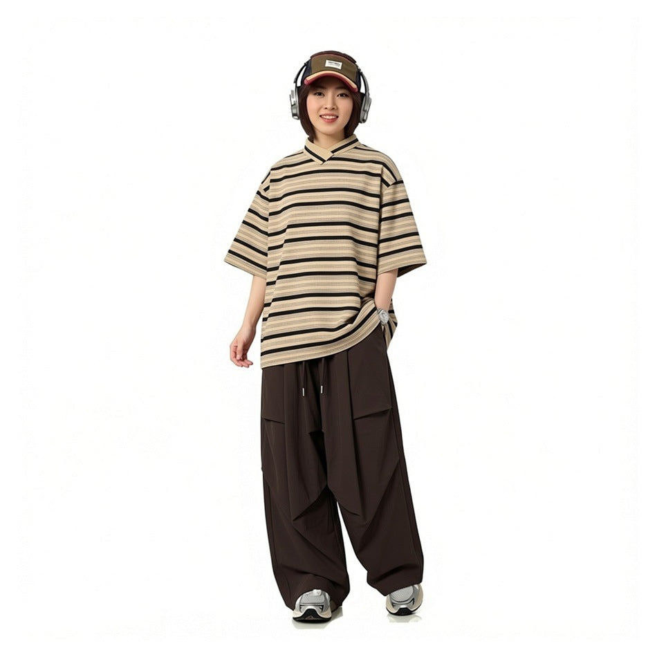 Model wearing an oversized beige-and-black striped V-neck shirt and wide dark brown trousers.