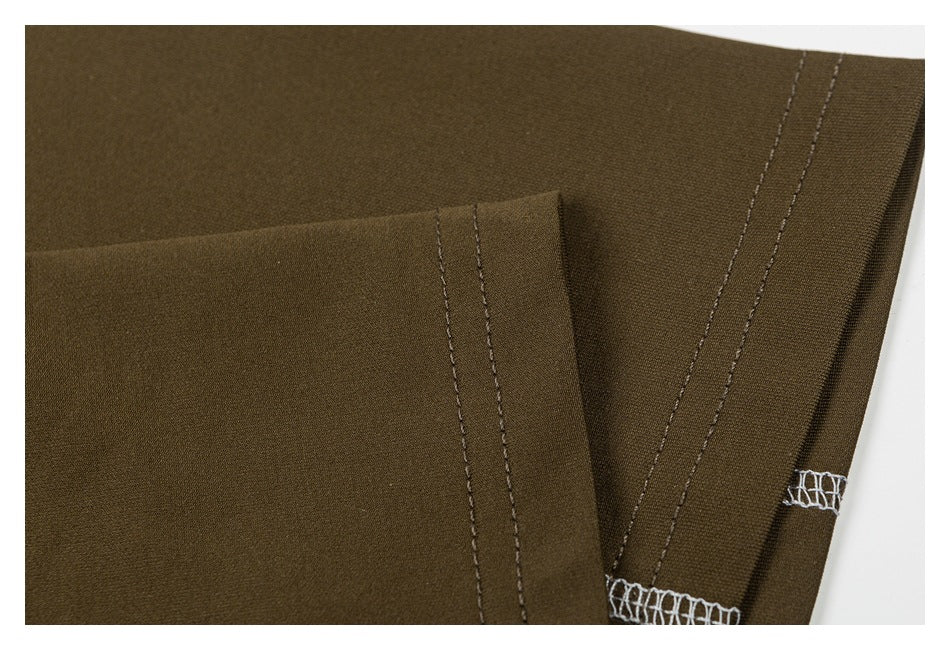 Close-up of olive garment construction showing folded edges, parallel stitching, and white overlock seams.