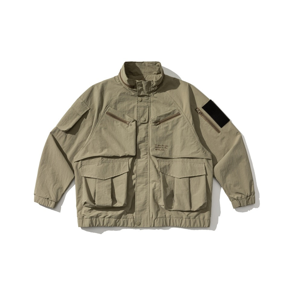 Khaki stand-collar utility jacket flat lay with large flap pockets, zip chest pockets and black sleeve patch