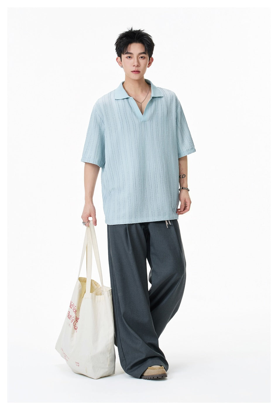 Model wearing a sky blue textured-stripe short-sleeve V-neck polo top with gray wide-leg pants, holding a tote bag
