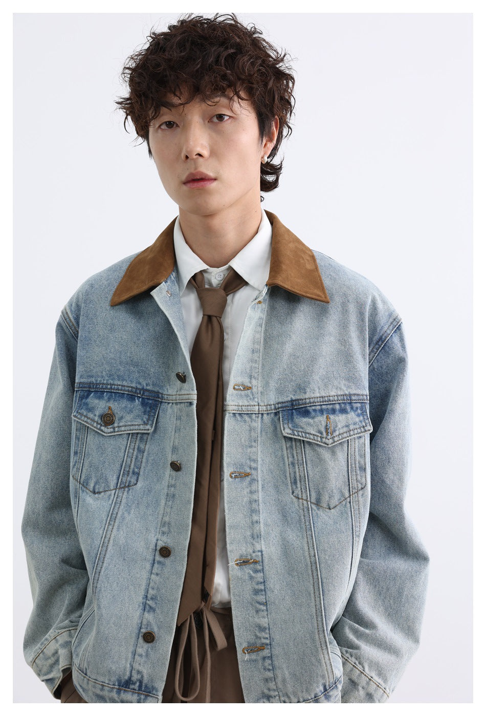 Model wearing a light-wash denim jacket with a brown collar over a white shirt and brown tie.