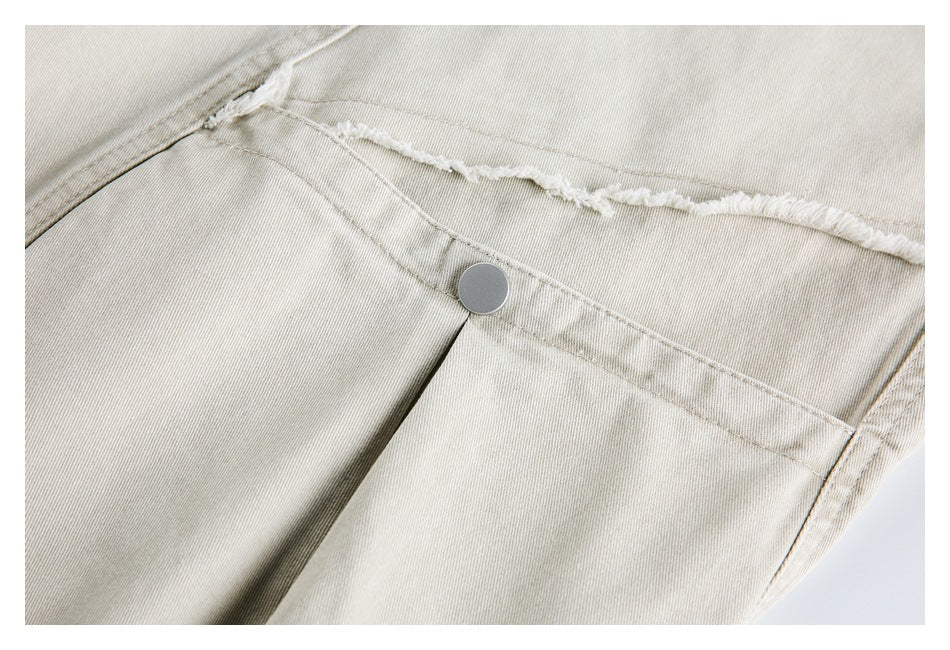 Close-up of light beige trousers showing a metal button, pocket seam and frayed edge.