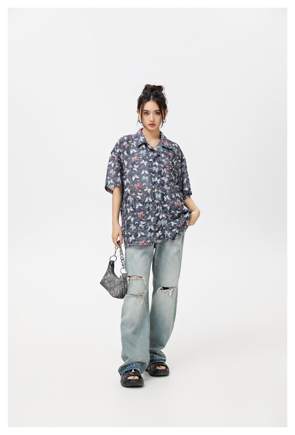 Model wearing an oversized navy butterfly-print button-up shirt with ripped light-wash jeans.