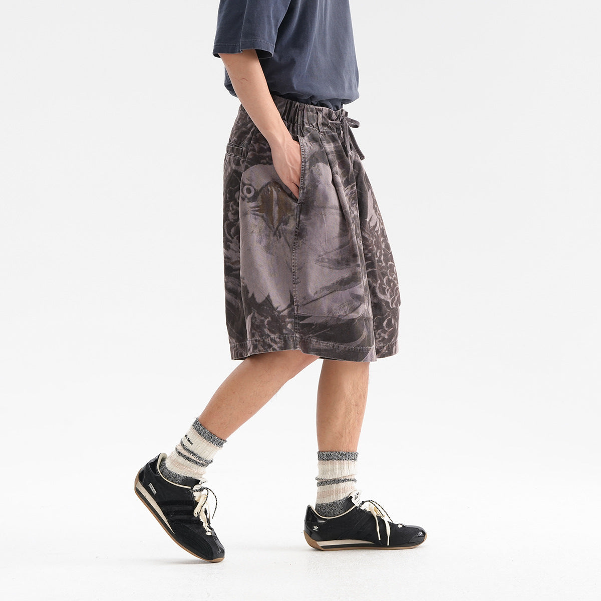 Side view of a model wearing loose charcoal-gray graphic shorts with an elastic drawstring waist and large side pockets.