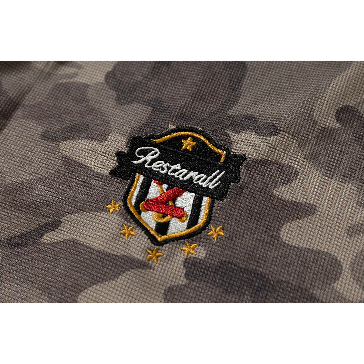 Close-up of an embroidered black, gold, red, and white crest on gray-brown camouflage fabric.