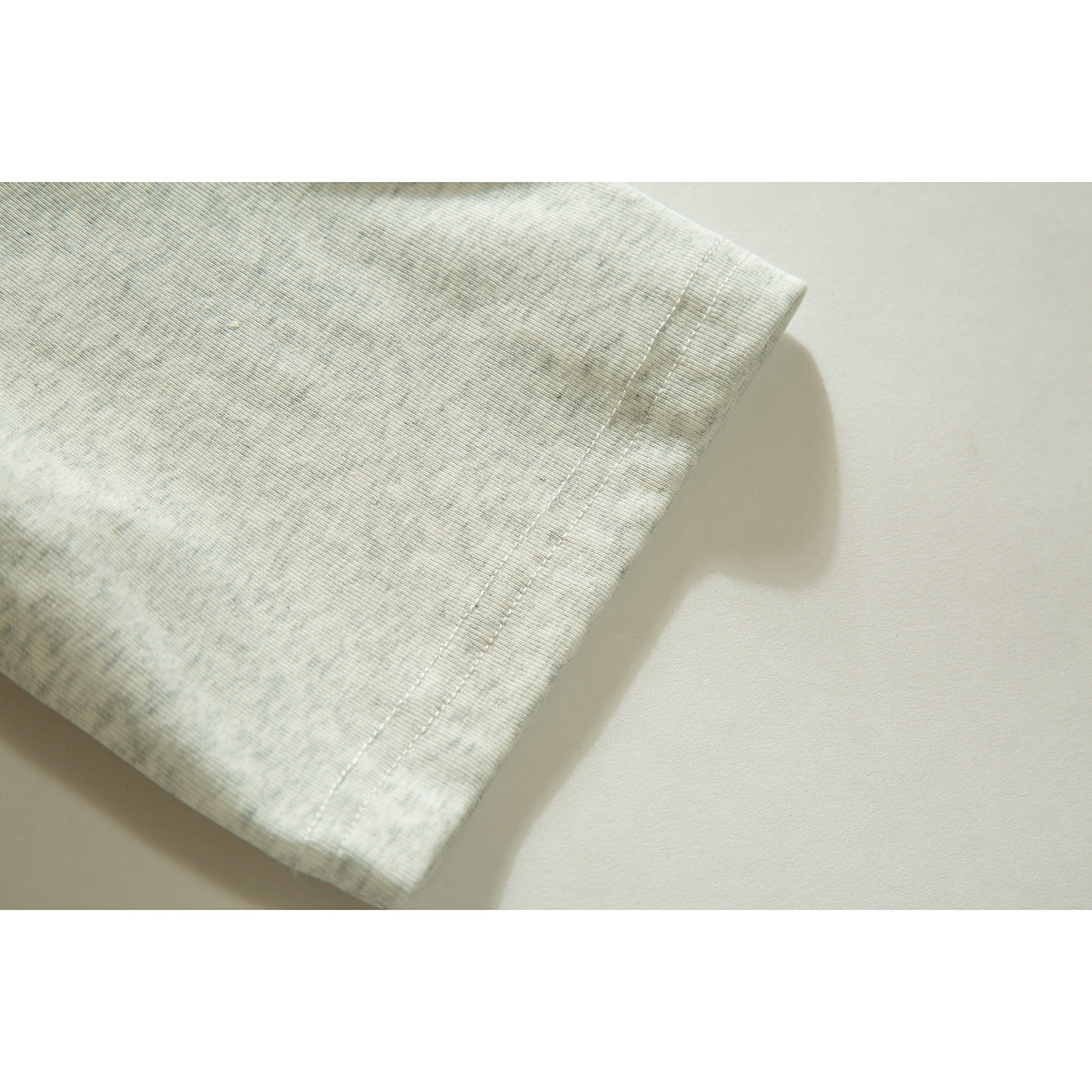 Close-up of the double-stitched hem on a light gray heathered polo shirt.