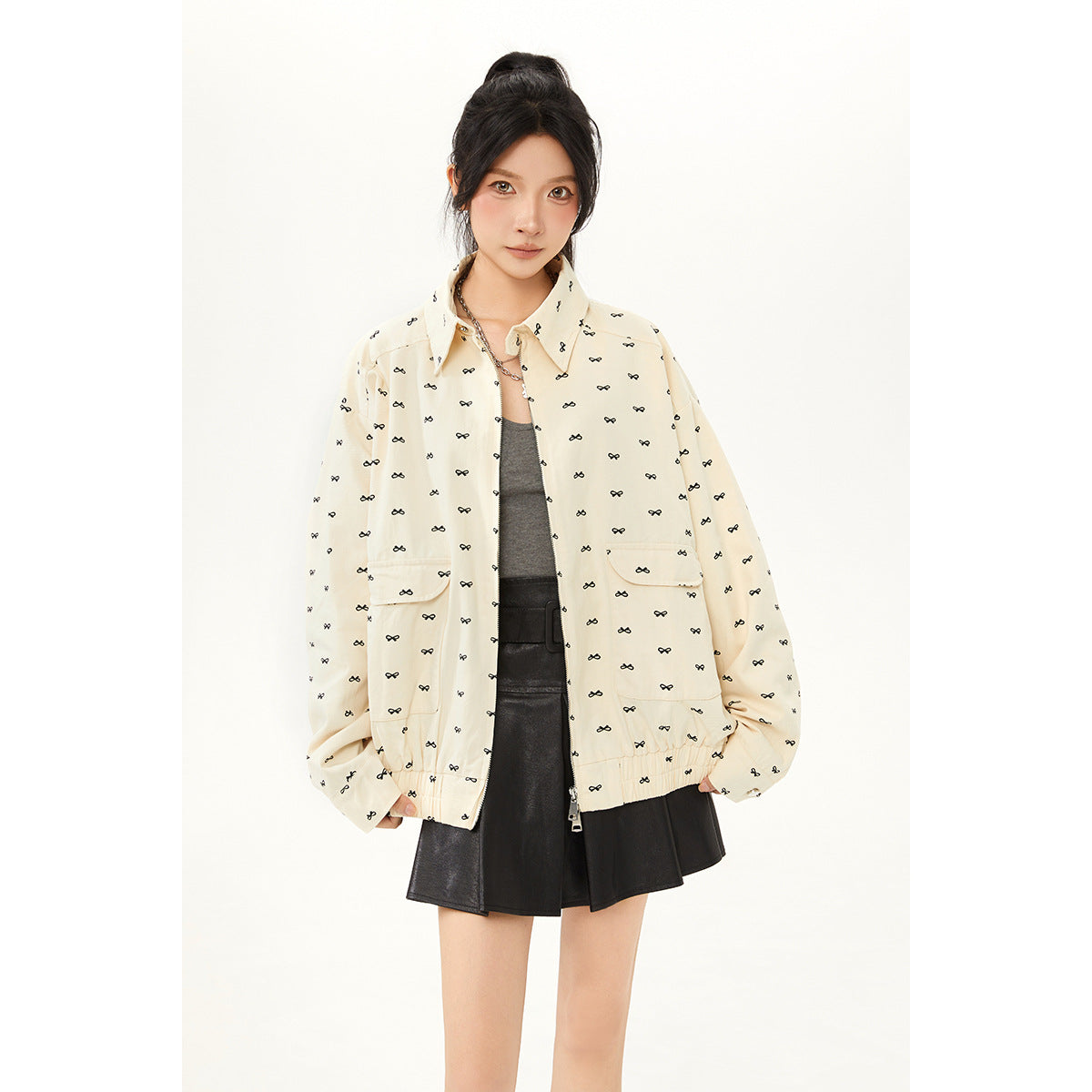Model wearing a cream jacket with small black bow motifs, a gray top, and a black skirt; front view.