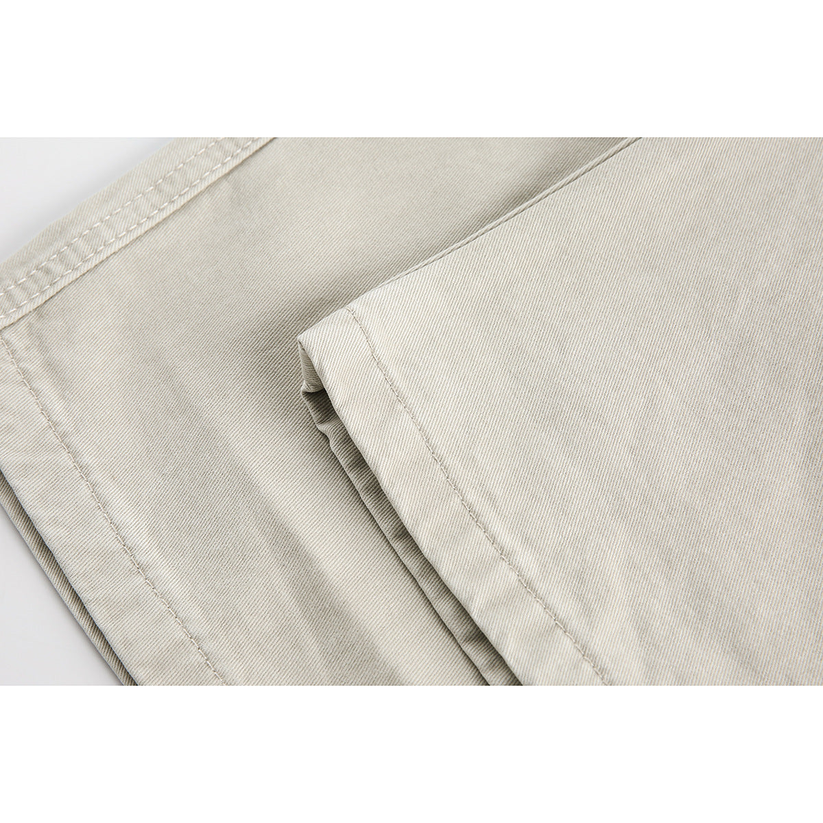 Close-up of light beige pants fabric, folded leg panels, and stitching.