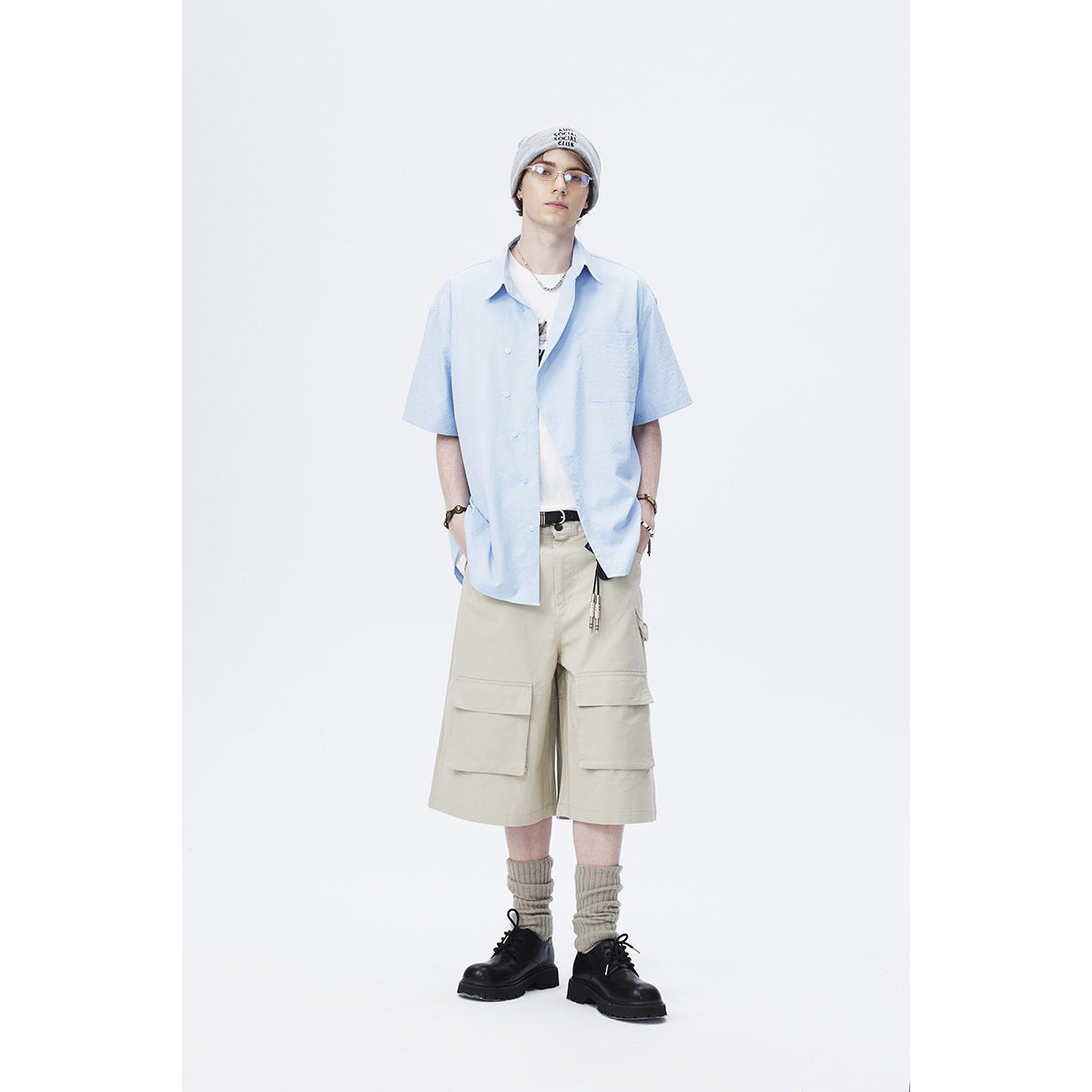 Model wearing a light blue short-sleeve button-up shirt with a chest pocket, styled with beige cargo shorts.