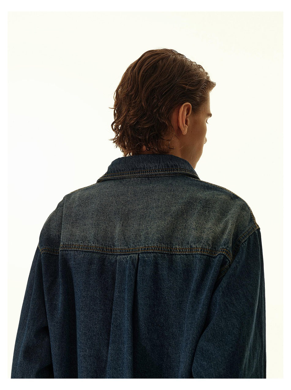 Close-up of the back of a dark indigo denim shirt, showing its lighter faded yoke, collar, and shoulder seams.